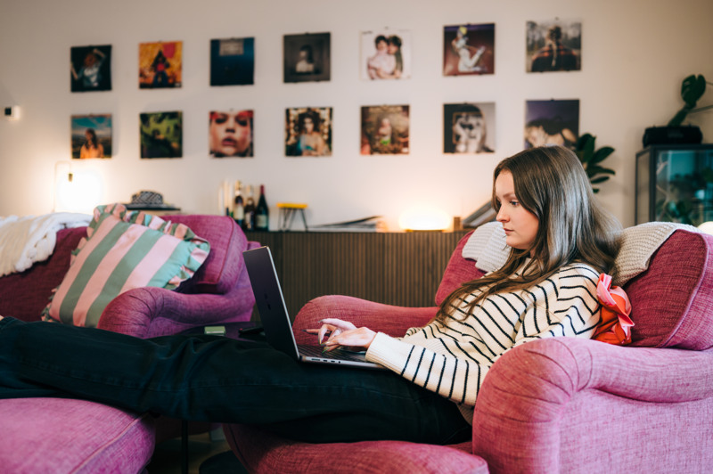 En kvinna sitter i en soffa och anv&auml;nder en b&auml;rbar dator.