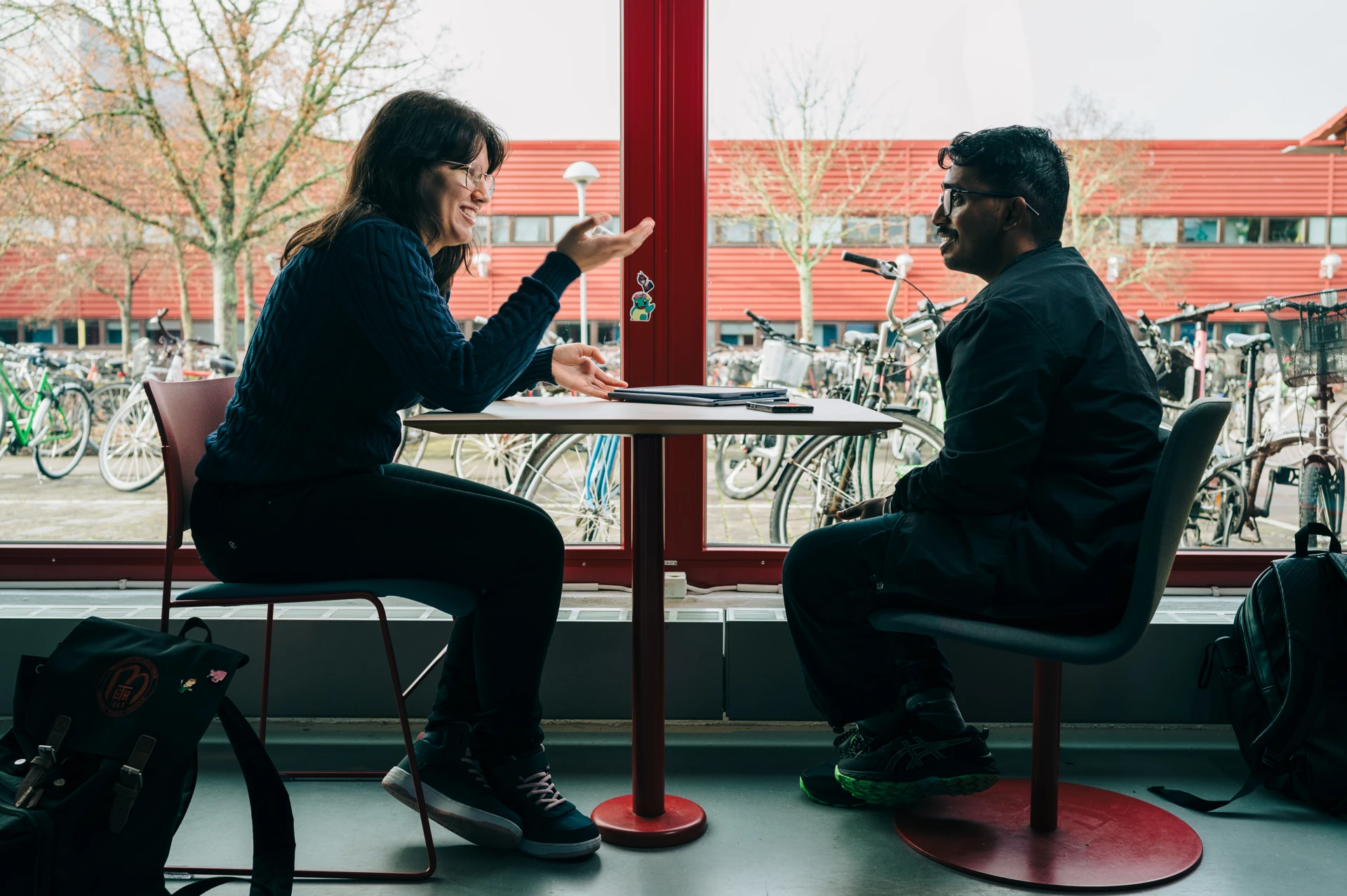 A man and a woman sitting at a table in front of a window.