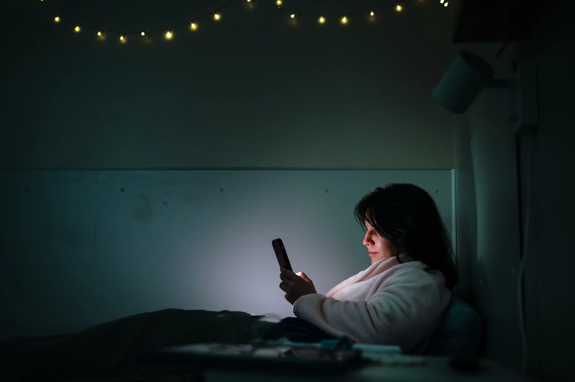 A woman sitting in bed looking at a cell phone.