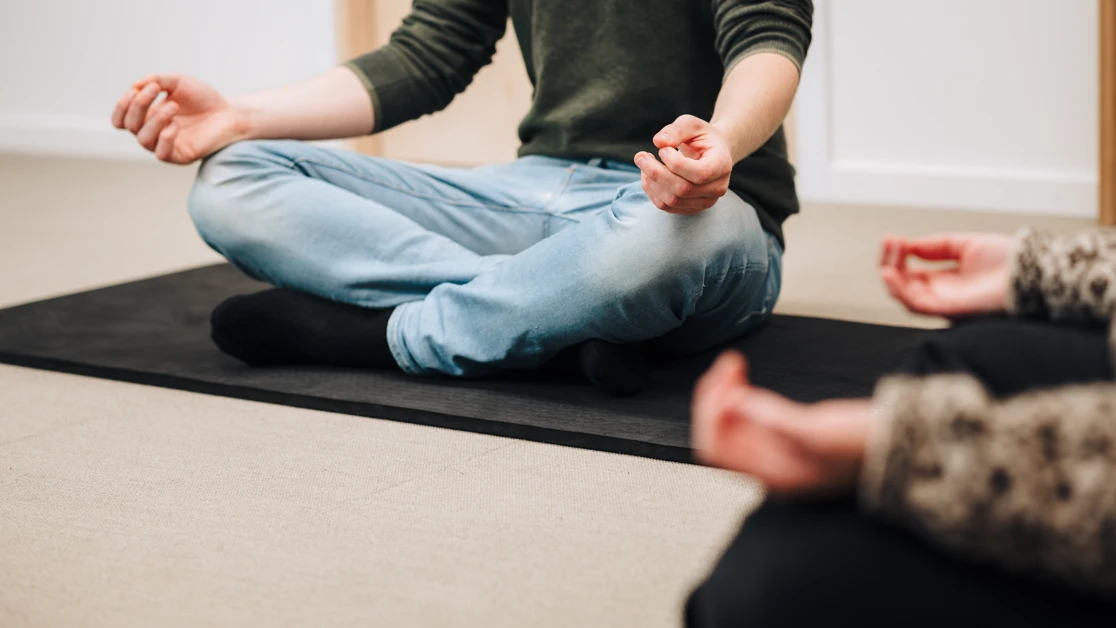 En man sitter i lotusställning på en yogamatta